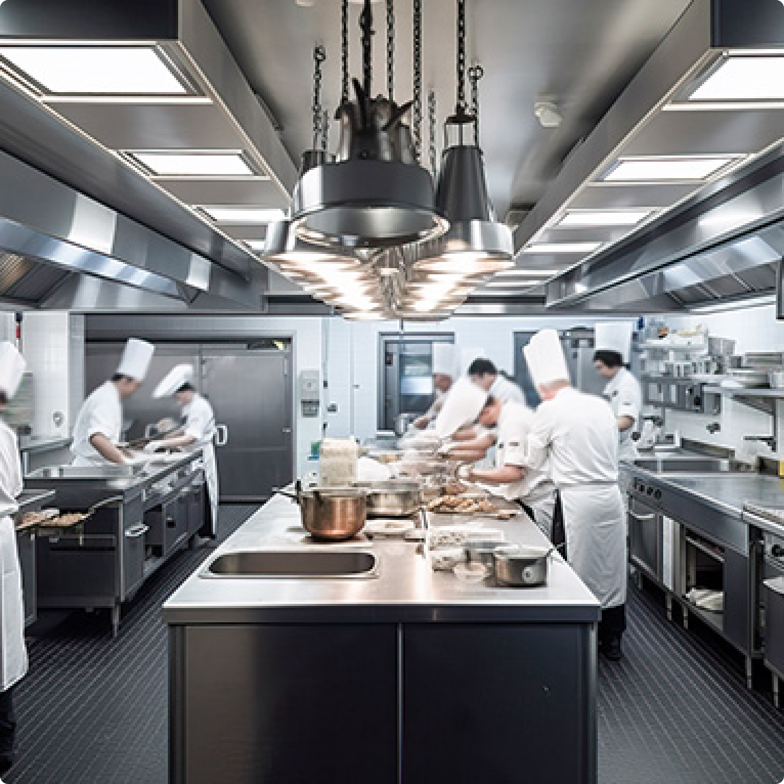 Professional chefs working in a modern stainless steel commercial kitchen, preparing food on large counters with cooking equipment and utensils.